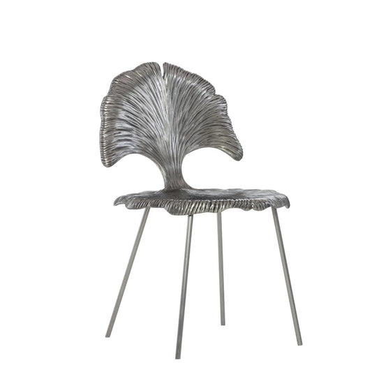 A modern sculptural side chair with a metallic silver seat and backrest featuring a textured, fan-like leaf design, supported by slim metal legs, shown against a plain white background.