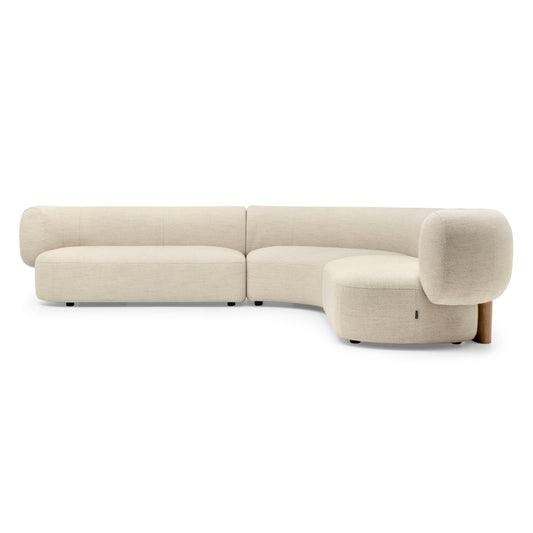 A modern curved modular sofa upholstered in a light beige textured fabric, featuring a low-profile design with cylindrical armrests and dark wooden legs, shown against a plain white background.