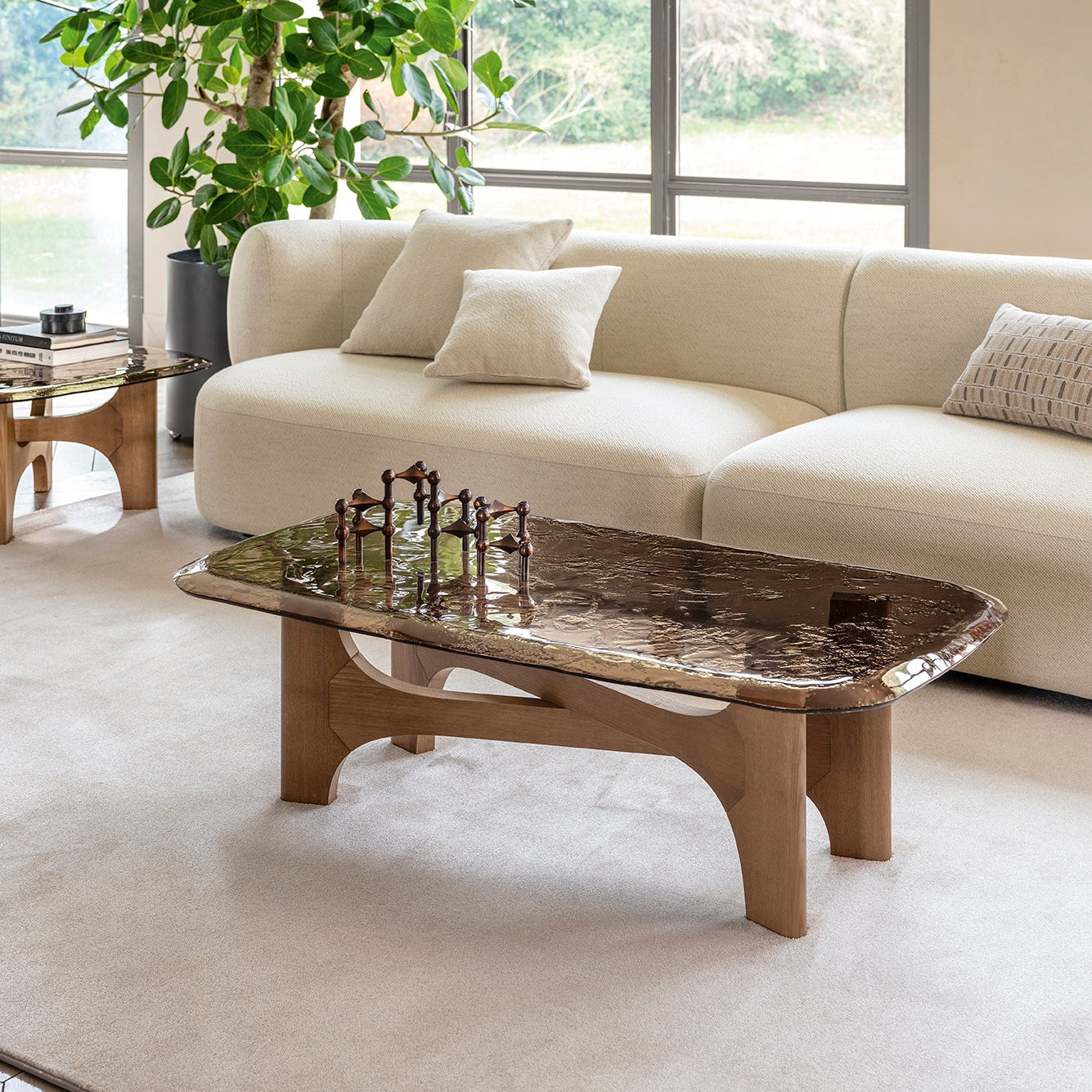 A modern living room scene featuring a rectangular coffee table with a dark, polished stone top and a light wood base, set on a large cream-colored rug in front of a beige sofa.